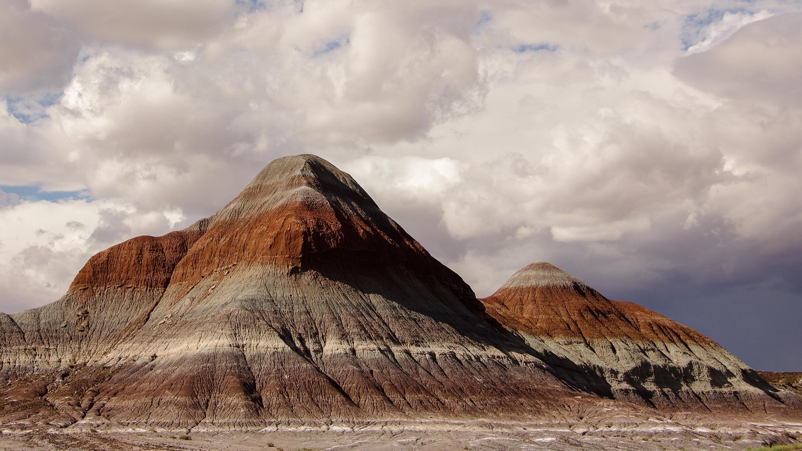 Red and gray badland hills against a mostly cloudy sky.