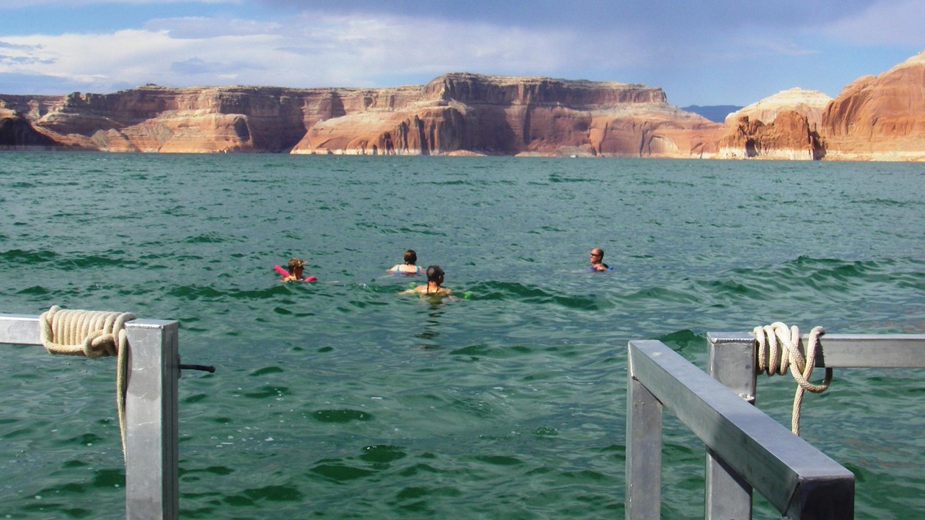 Four people swim backwards away from a houseboat railing