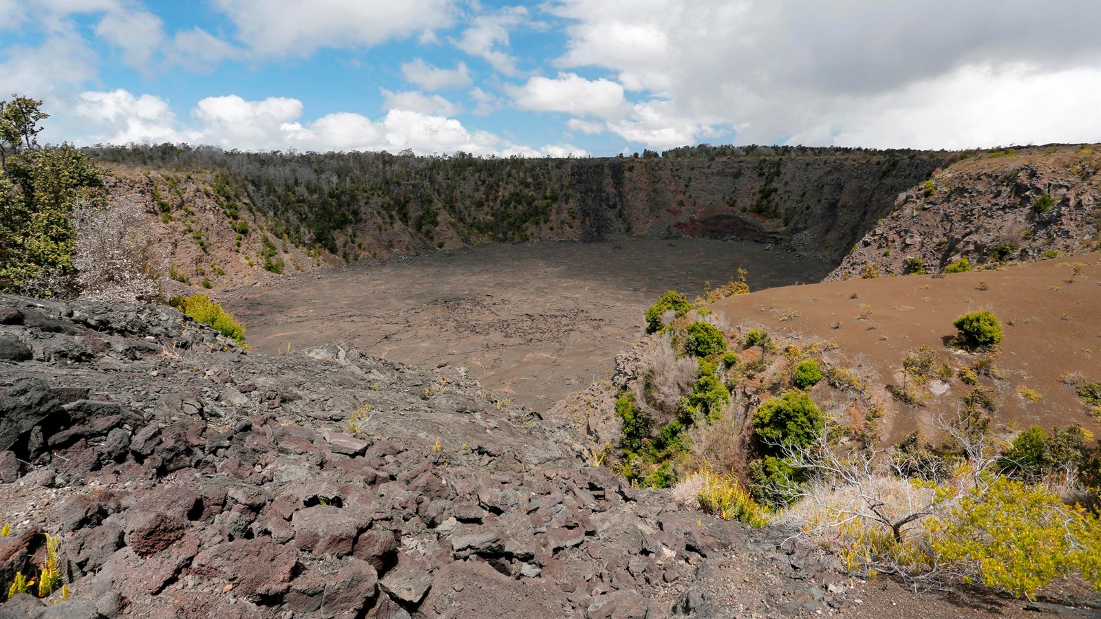 A volcanic pit crater surrounded by cinders and small trees.
