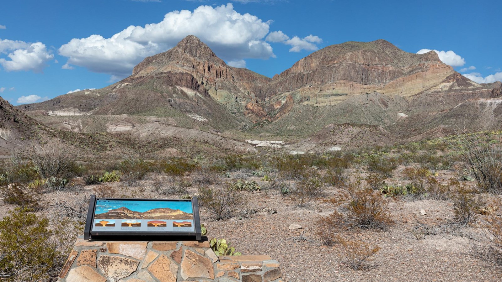 A metal exhibit atop a rock pedestal is situated at the base of a large mountain.