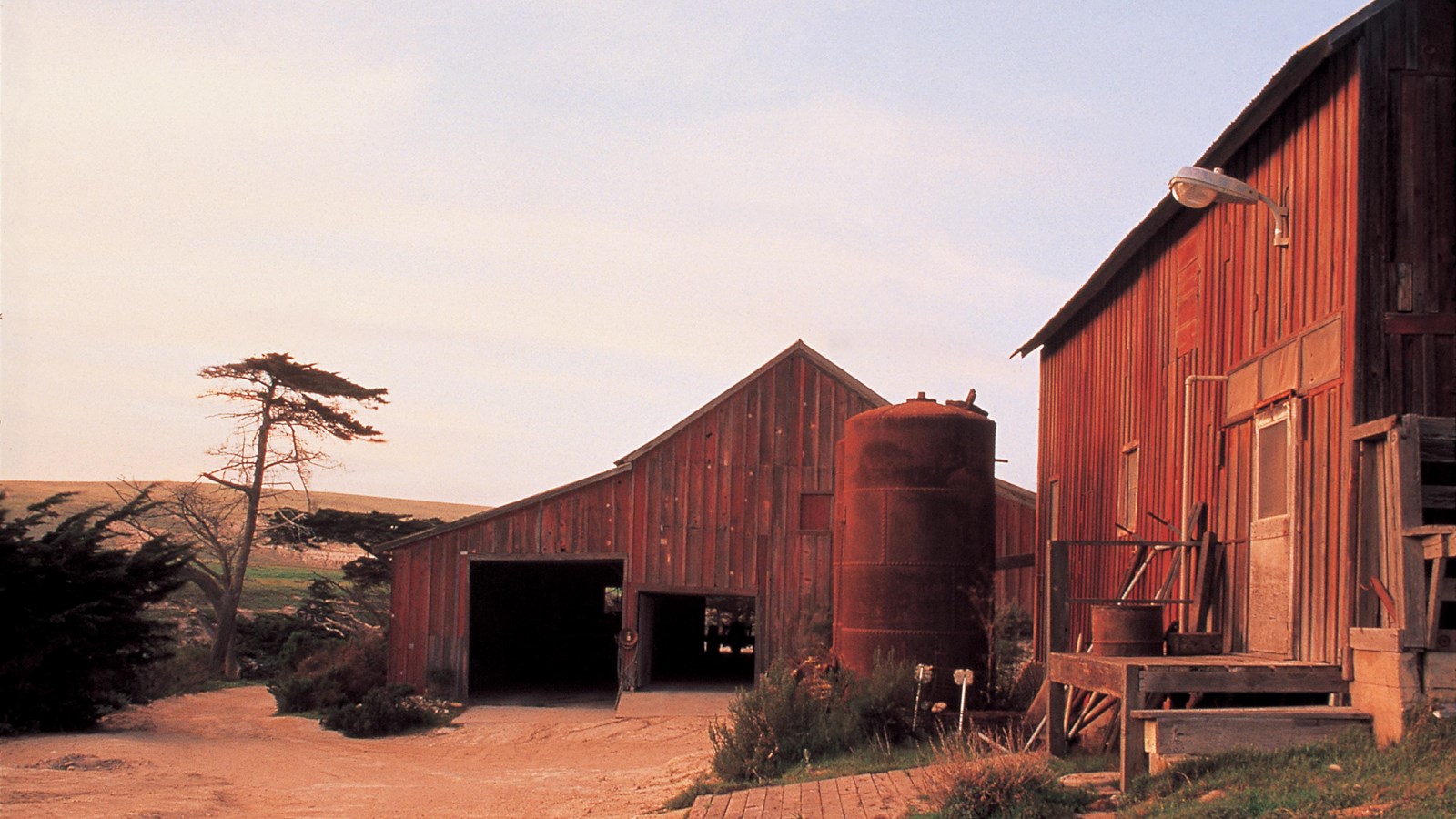 two old wood barns with two large vats next to them