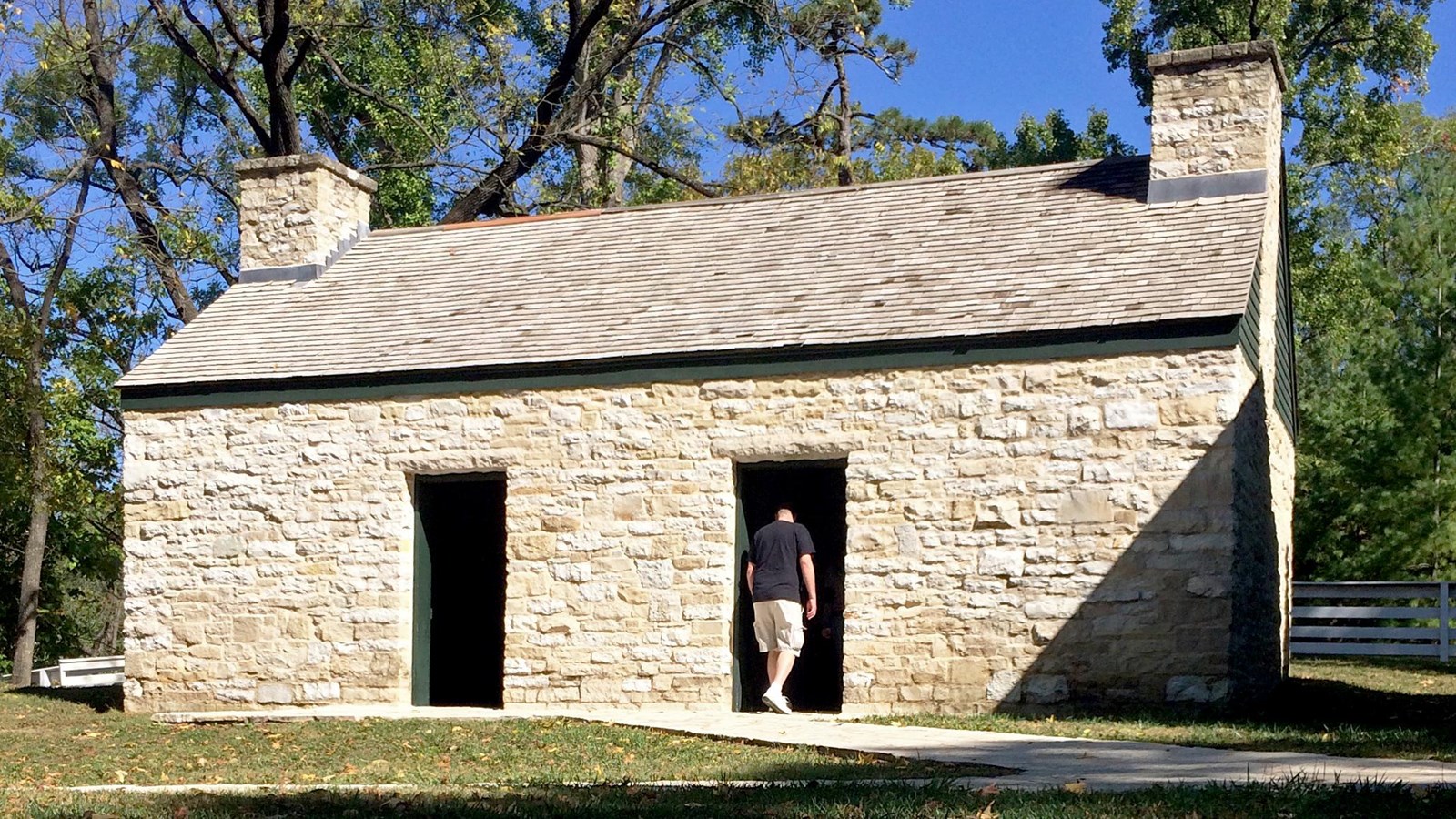 stone building with a chimney on each end. Two doors on long side. Man entering door on right.