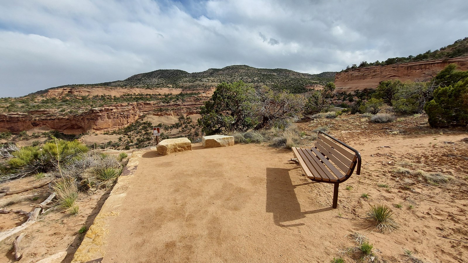 Bench along the right side of the crushed gravel trail. There is a scenic view of monolithes.