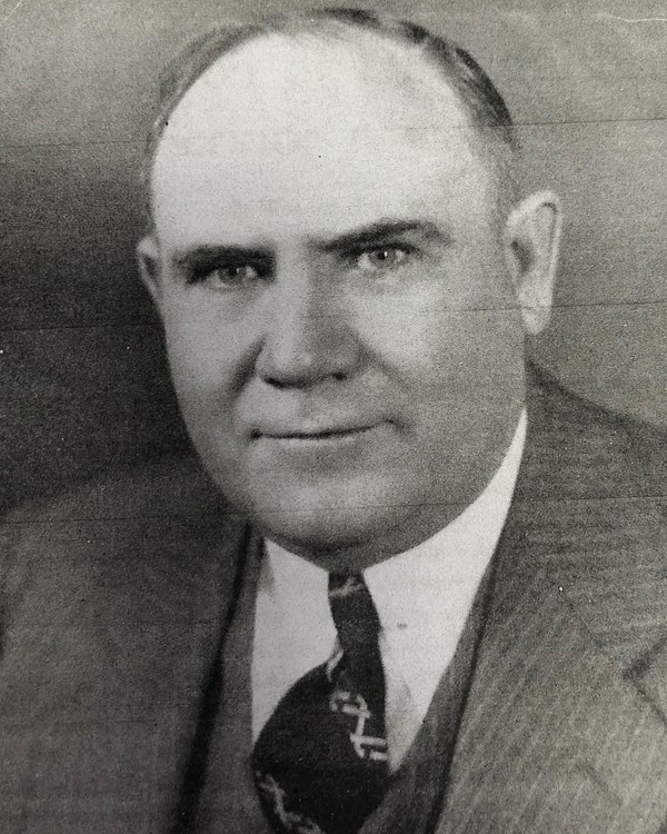 A black and white photo of a man dressed in a suit and tie