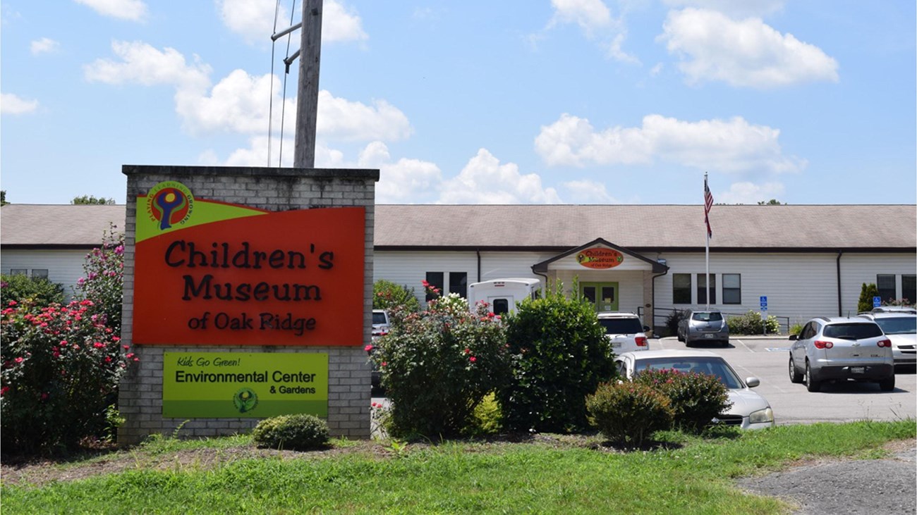 A large sign in front of a parking lot and school building.