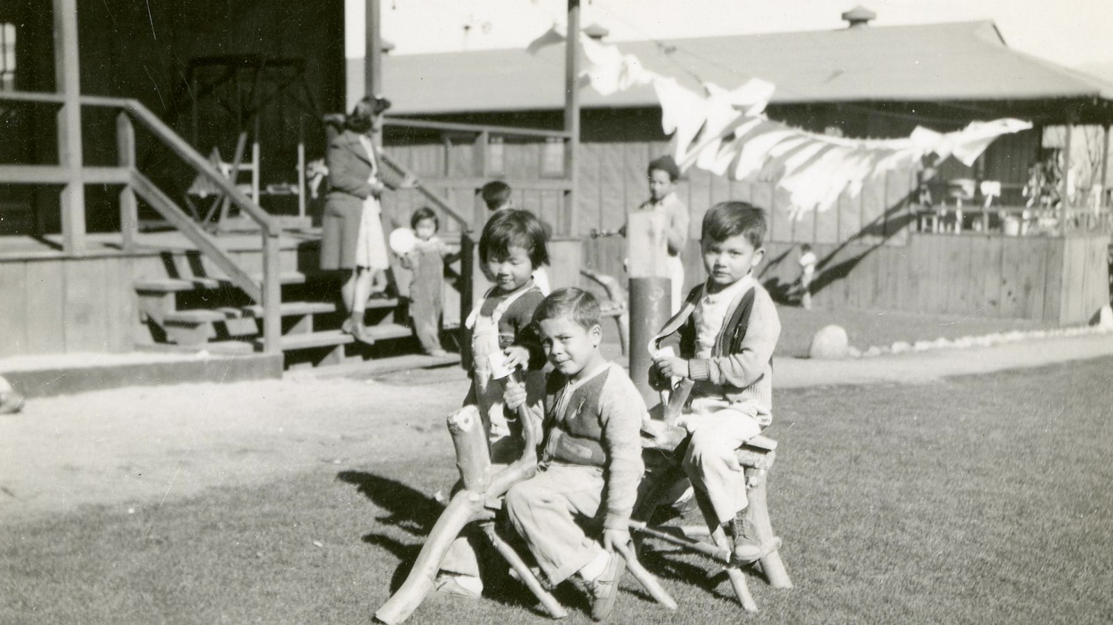 Black and white photo of children playing on a make-shift wooden horse outside