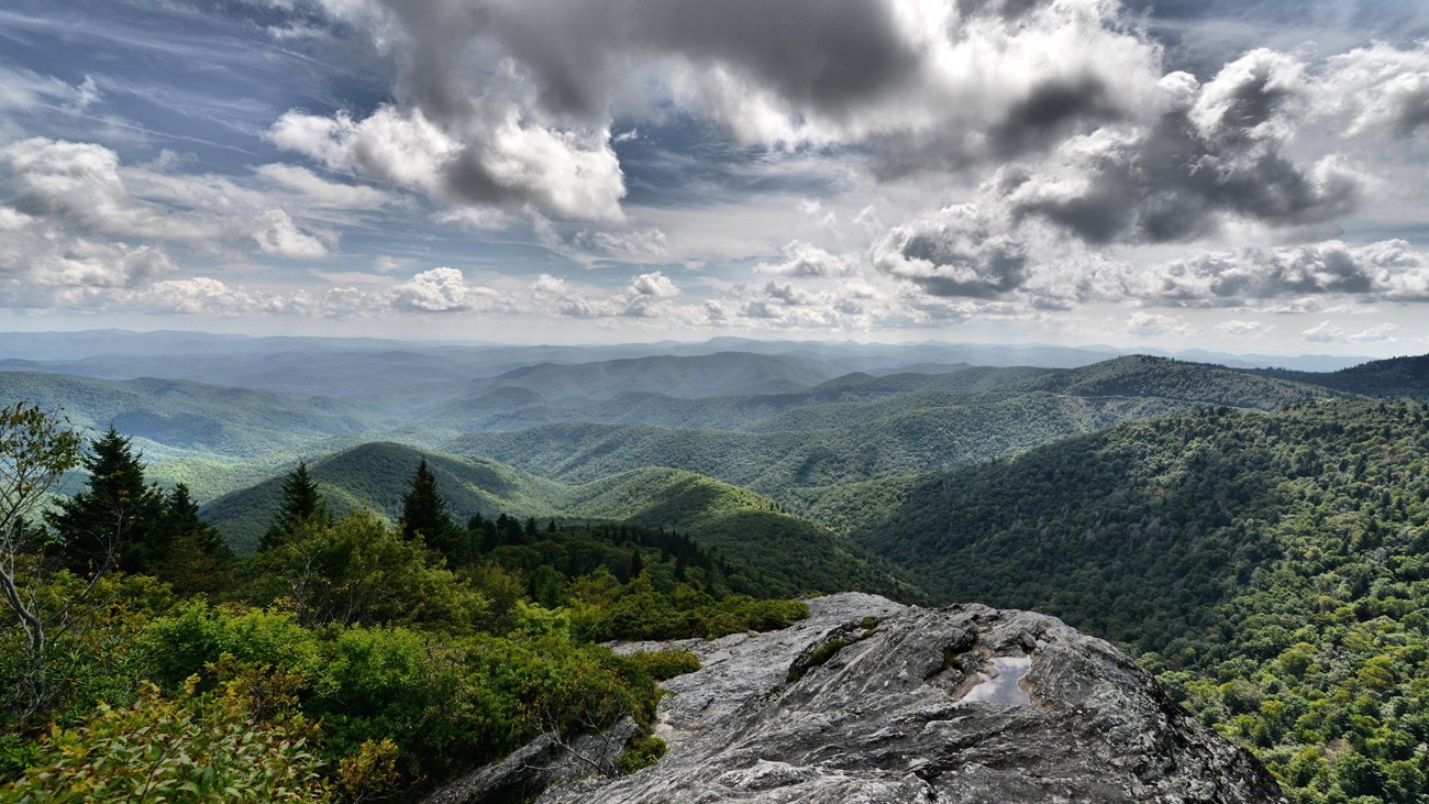 A rocky outcrop looks out over green layered mountains and white clouds