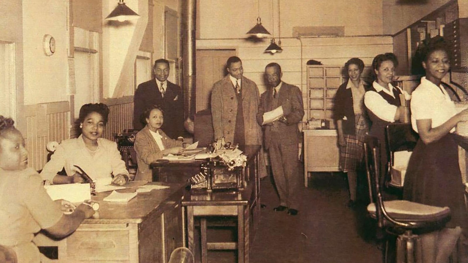 African American women and men dressed in business clothes are working in an office. 