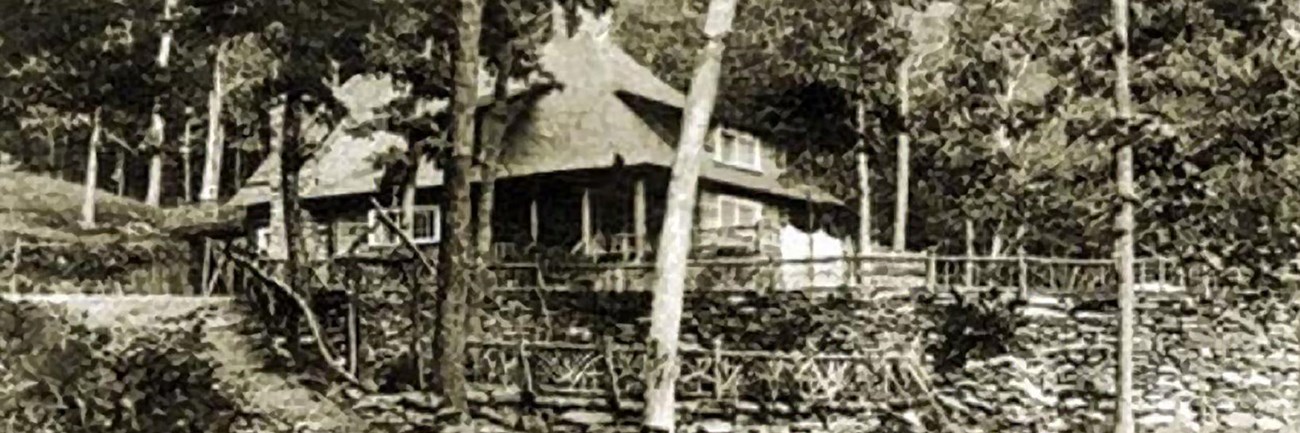 A historic black and white photo from the early 1900s of a rustic lodge in a forest.