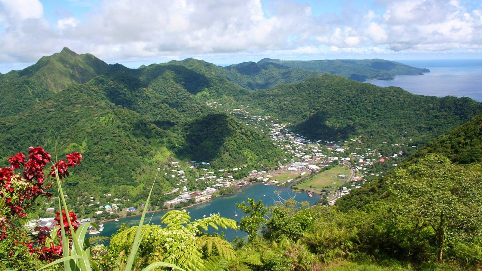 A lush group of mountains surrounded by ocean with a lakeside town nested in the mountain valley.