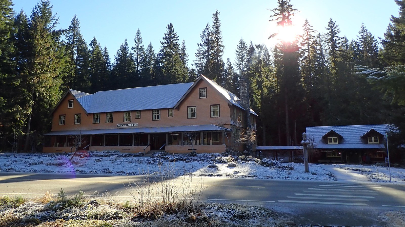 A two-story wood building with a small building next door, dusted by snow and surround by forest.
