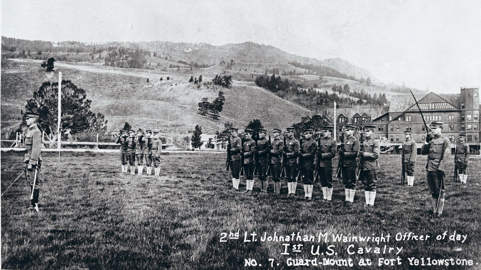 A historic photo of soldiers in uniform lining up on a grassy area in front of a hotel.