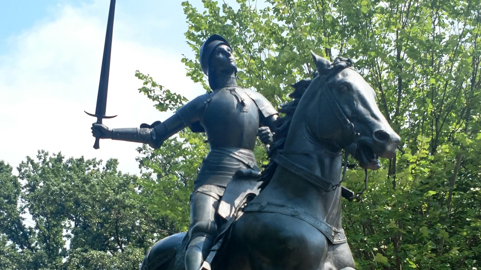 A bronze statue of Joan of Arc riding a horse, holding up a sword towards the sky
