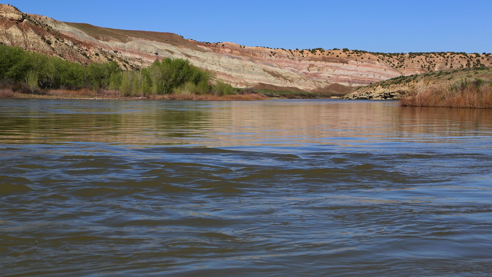 Ripples in a river as it flows towards colorful cliffs in the distance.