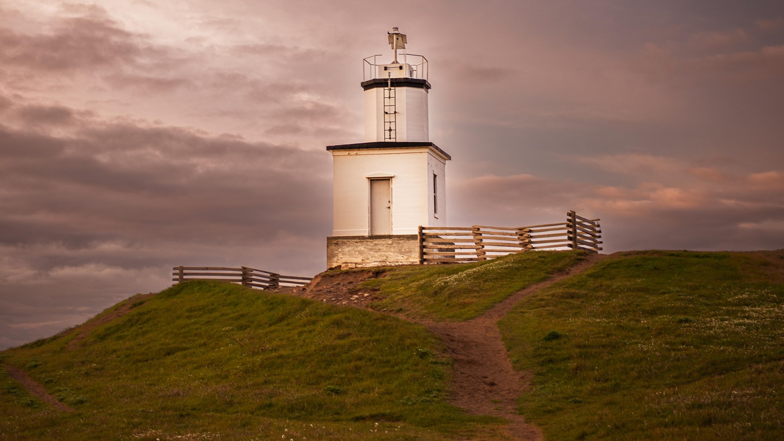 Color photograph of a white lighthouse with blazing light at sunset