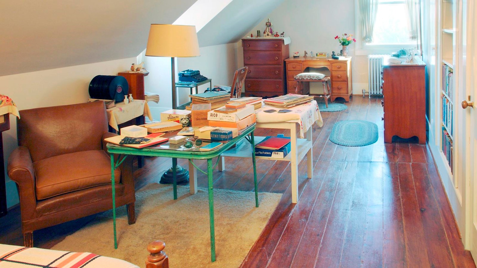 image of a bedrooms with bed, dresser, desk, books stacked on folding tables