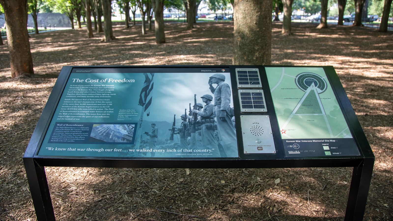 An information sign with text, photos, and a tactile map of the memorial area with braille labels.