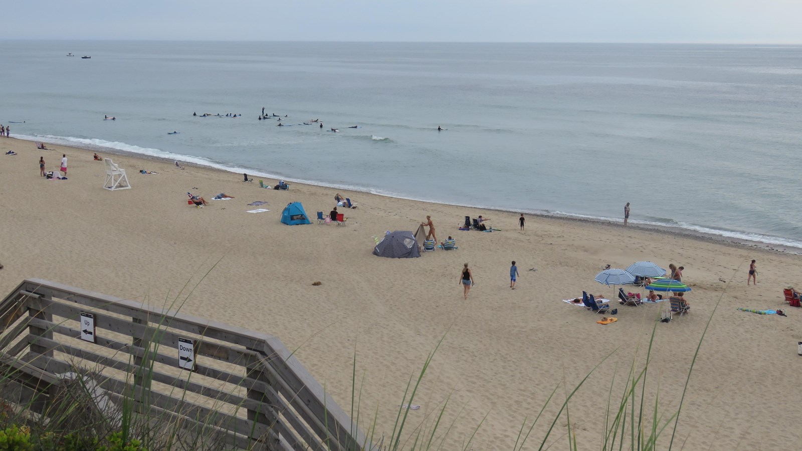 The landing of a stair is in the foreground with people on the beach and in the water below.