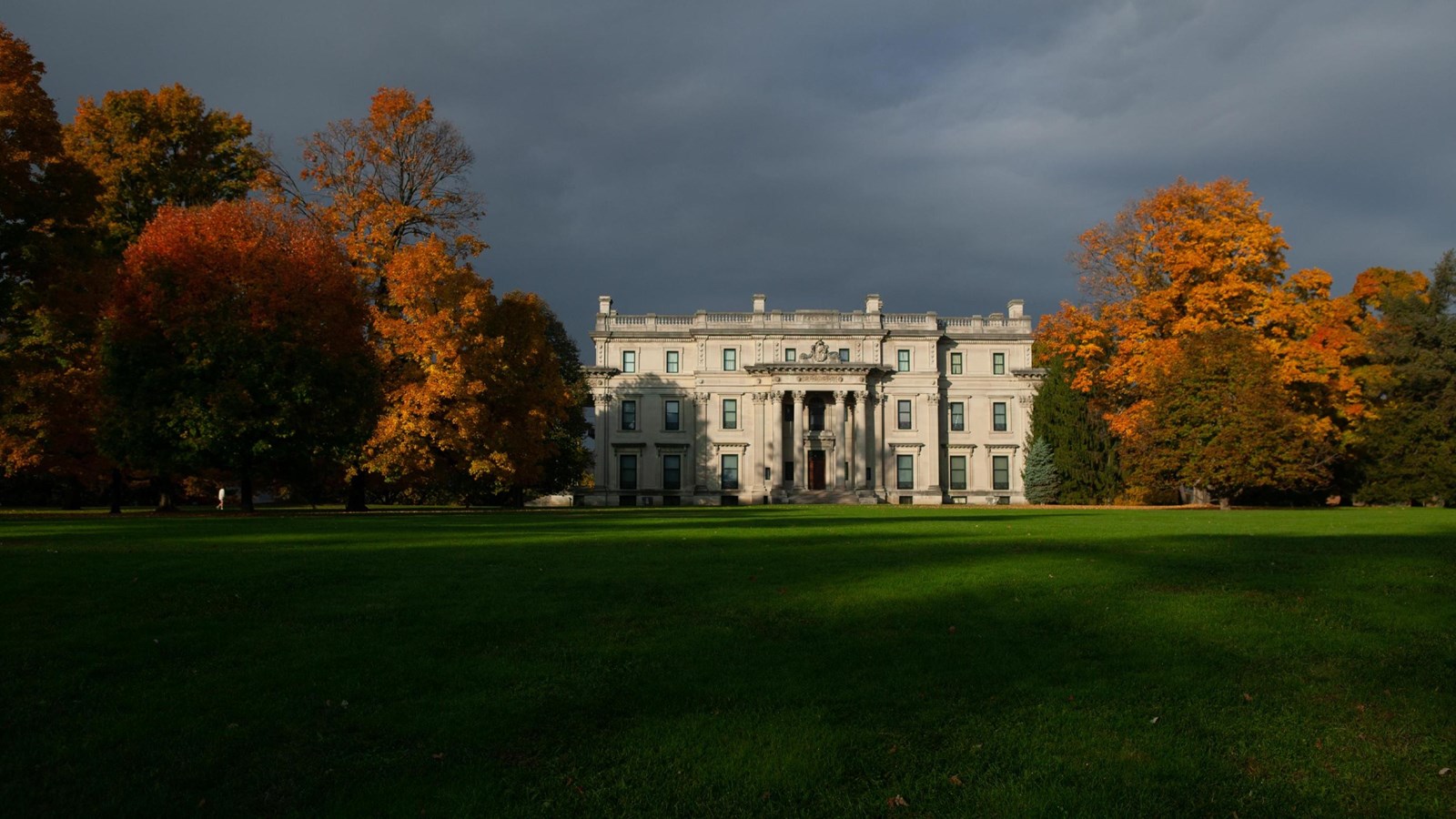 A very large, three story stone house with columns and central portico, set within a lush landscape.