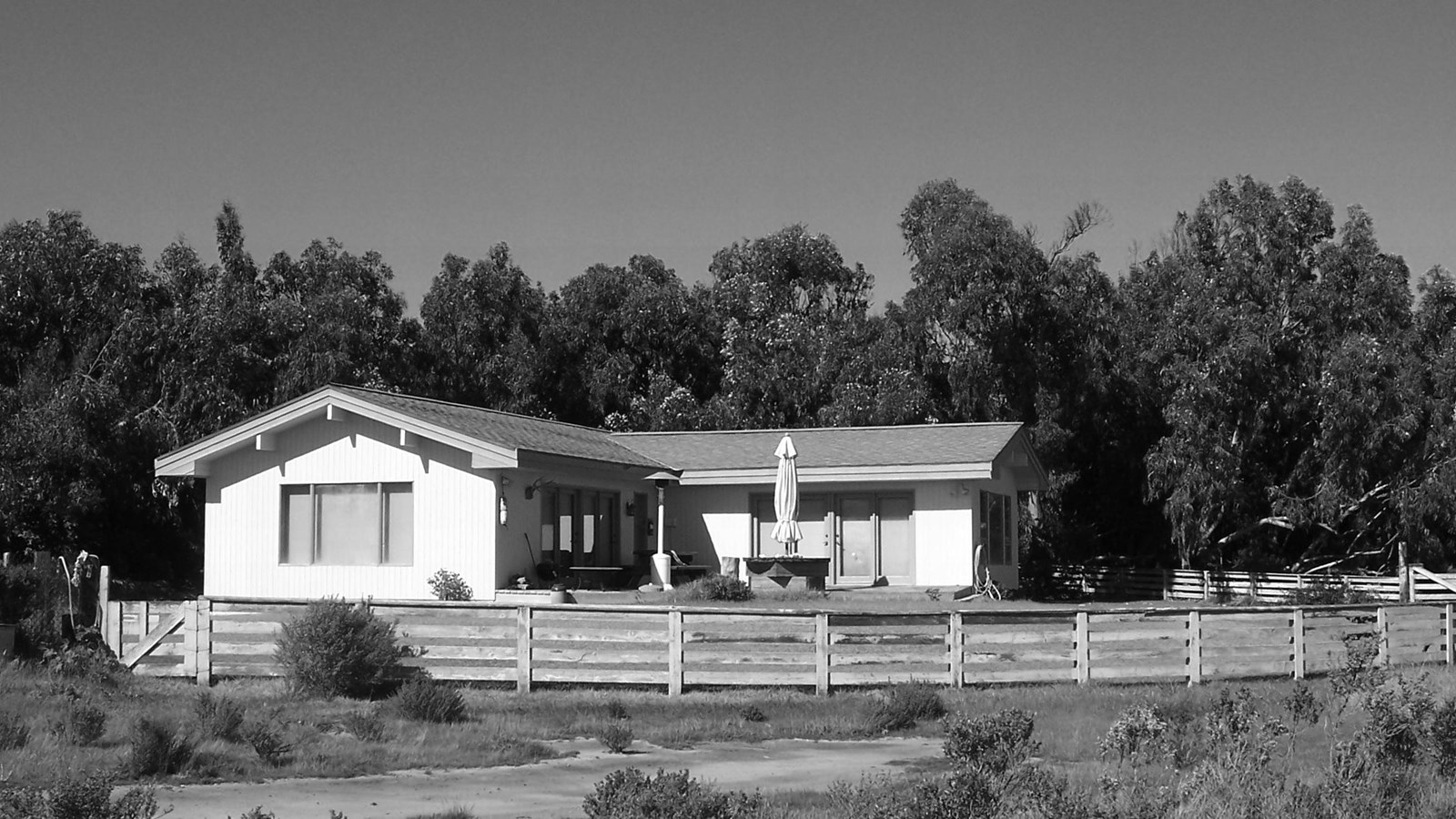 L shaped house with fence around it and trees behind it. 
