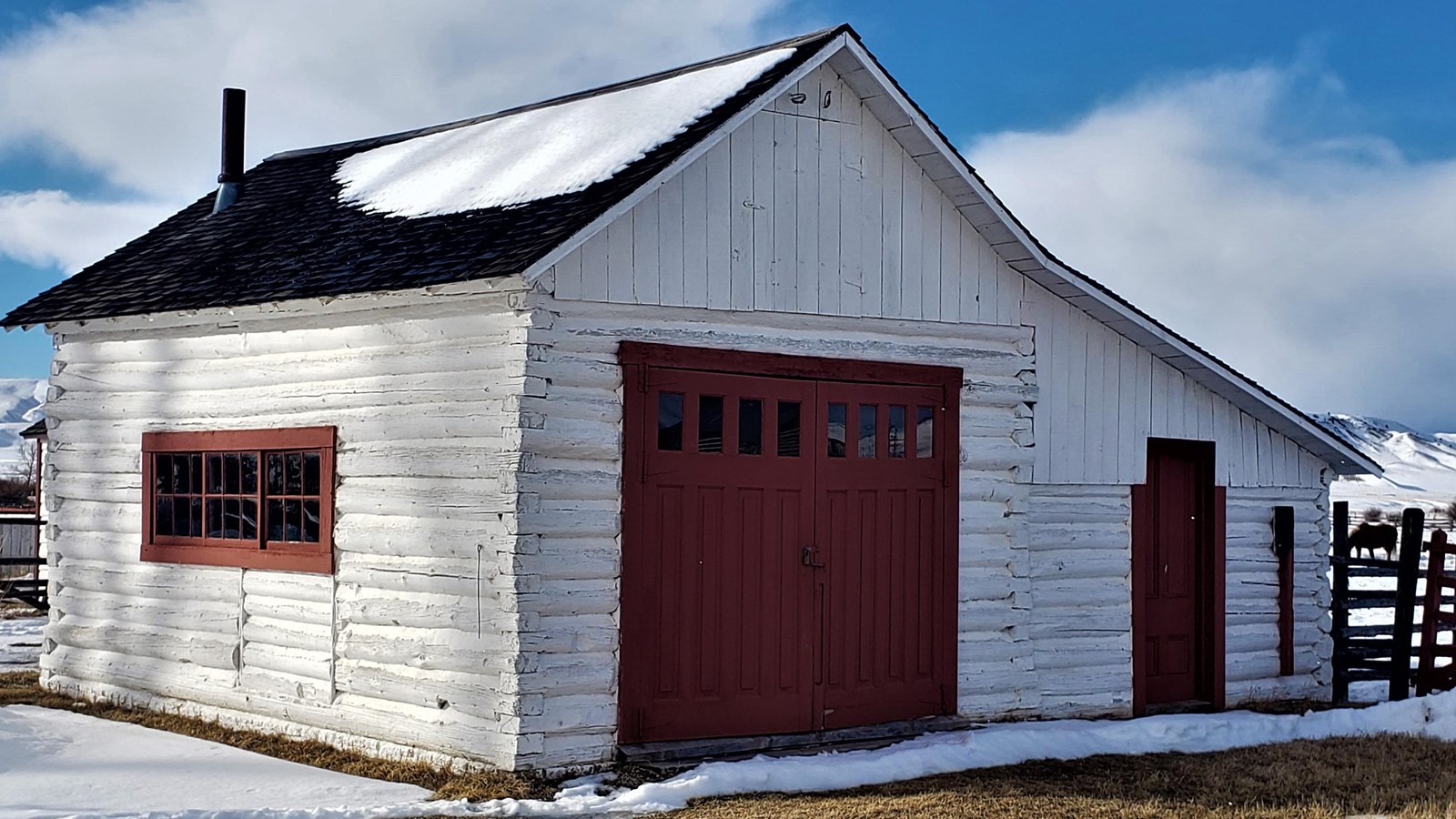 A white barn with a  large and small red door, a red roof, and windows surrounded by red trim.