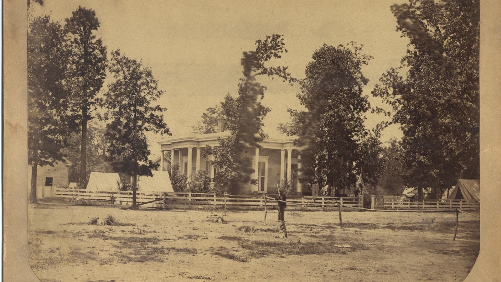 Historic image of a large house with columns and a soldier standing in the yard. 