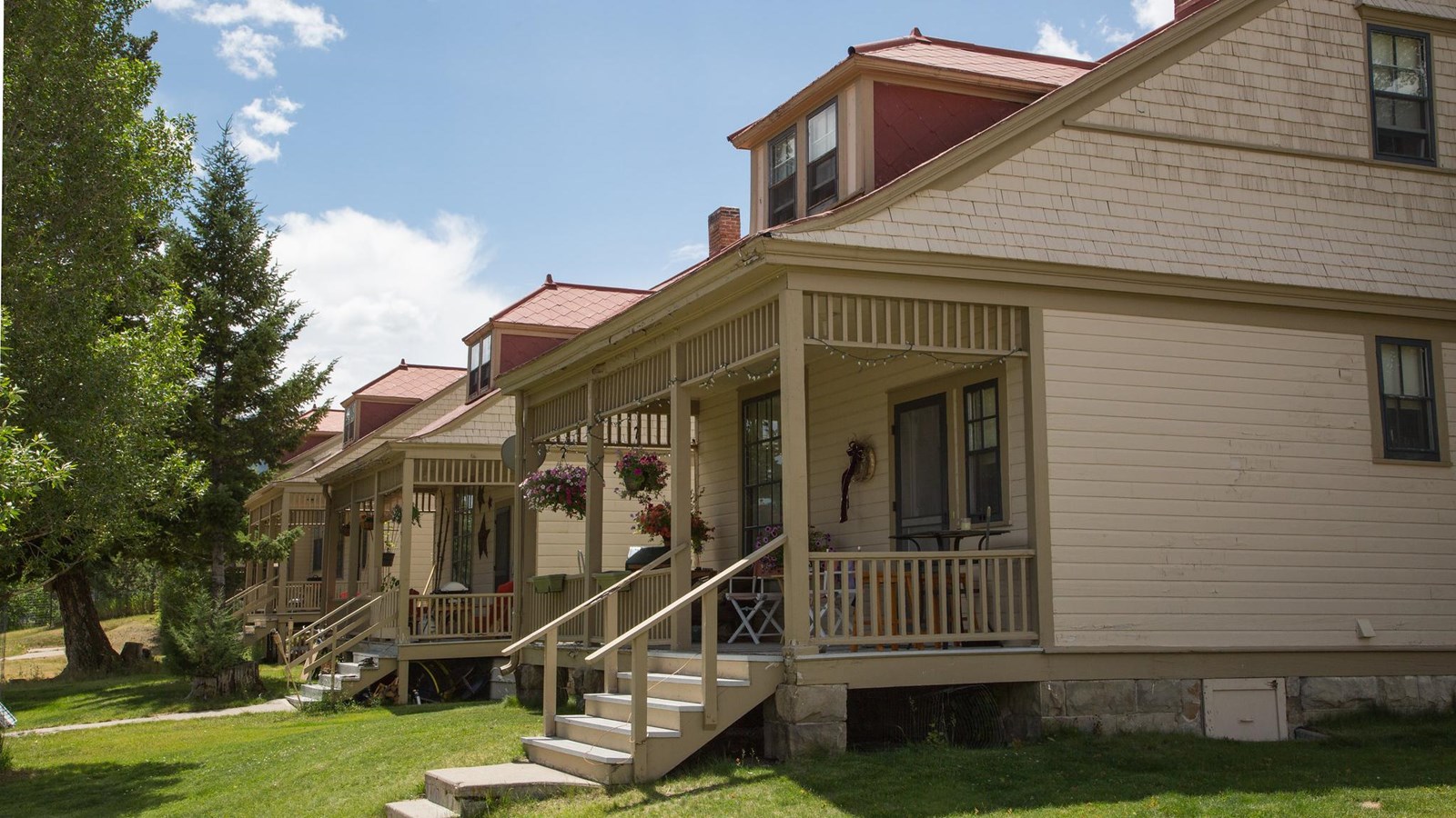 A historic building with pale, yellow siding, a red shingled roof, and a porch.