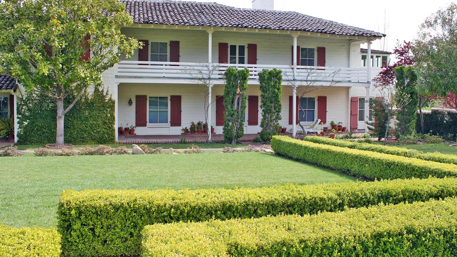 Two story historic home with upper and lower porches. Pathway shrubs create a walkway to back door.