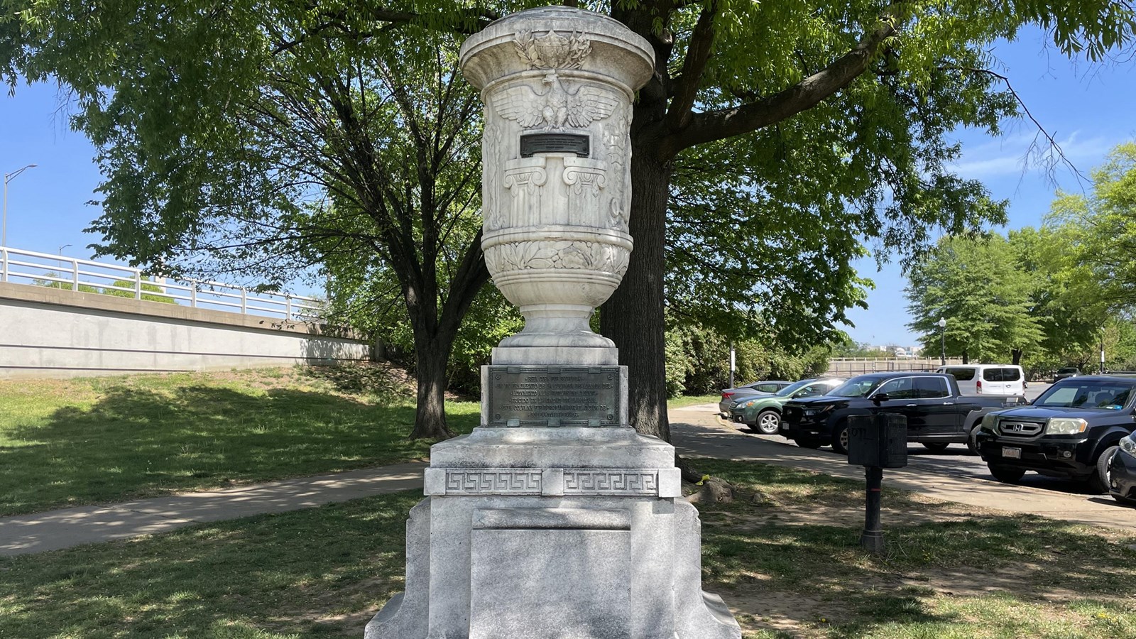 A large white, marble urn on a white pedestal with a tree in the background