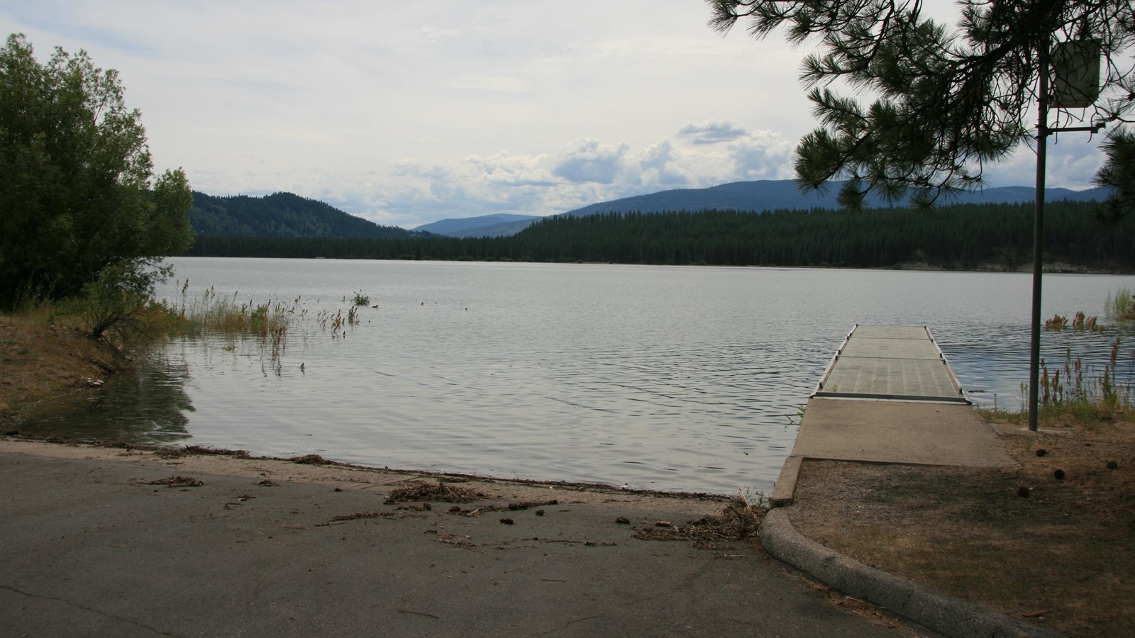 A paved boat ramp with a single floating dock, opening towards the lake and the mountains beyond.