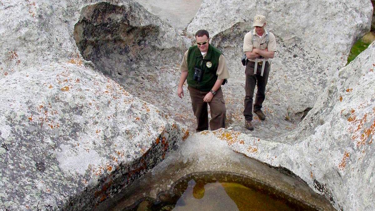 Two park rangers standing in a large dry panhole looking into a panhole filled with water.