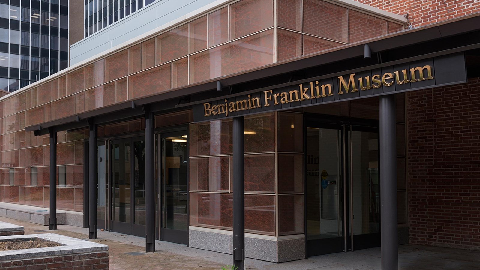 The exterior of a single story modern red building with an awning that says Benjamin Franklin Museum
