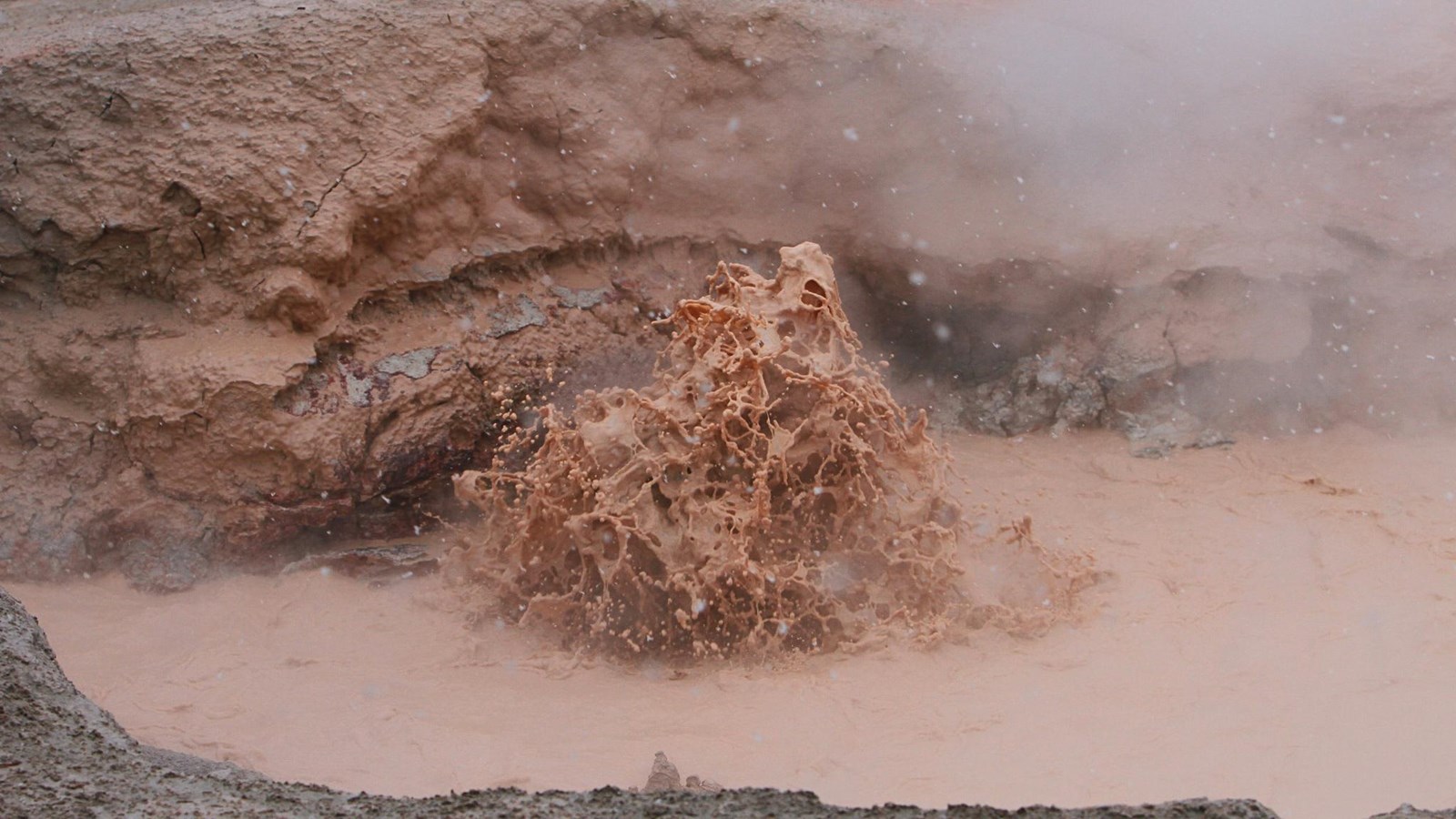 Muddy, red water splashes in a mudpot.