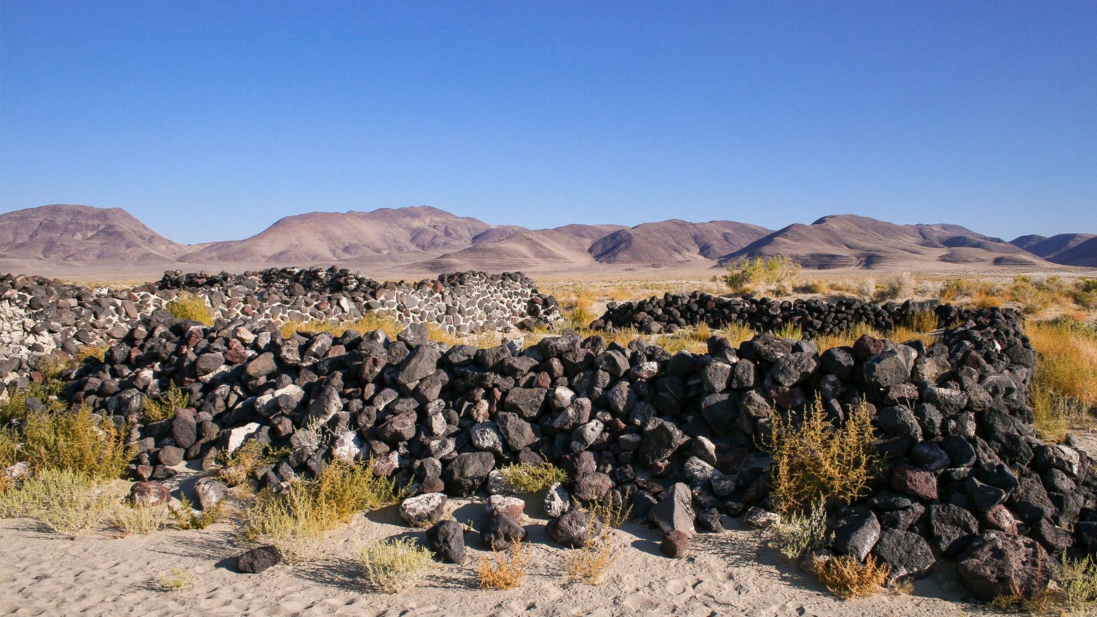 Walls made out of natural stacked red, white, and black rock rise several feet above a sandy area.