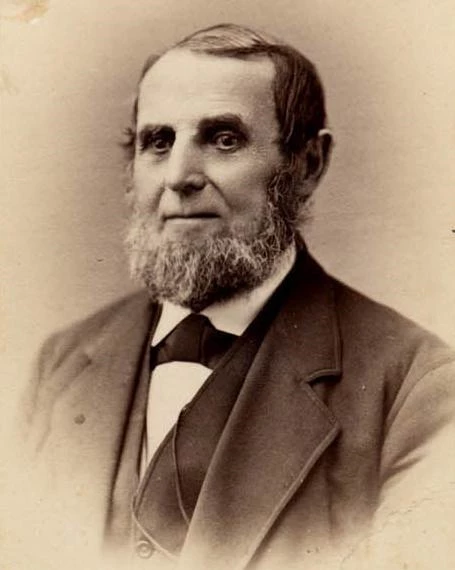 White man with a graying beard and a dark three-piece suit.