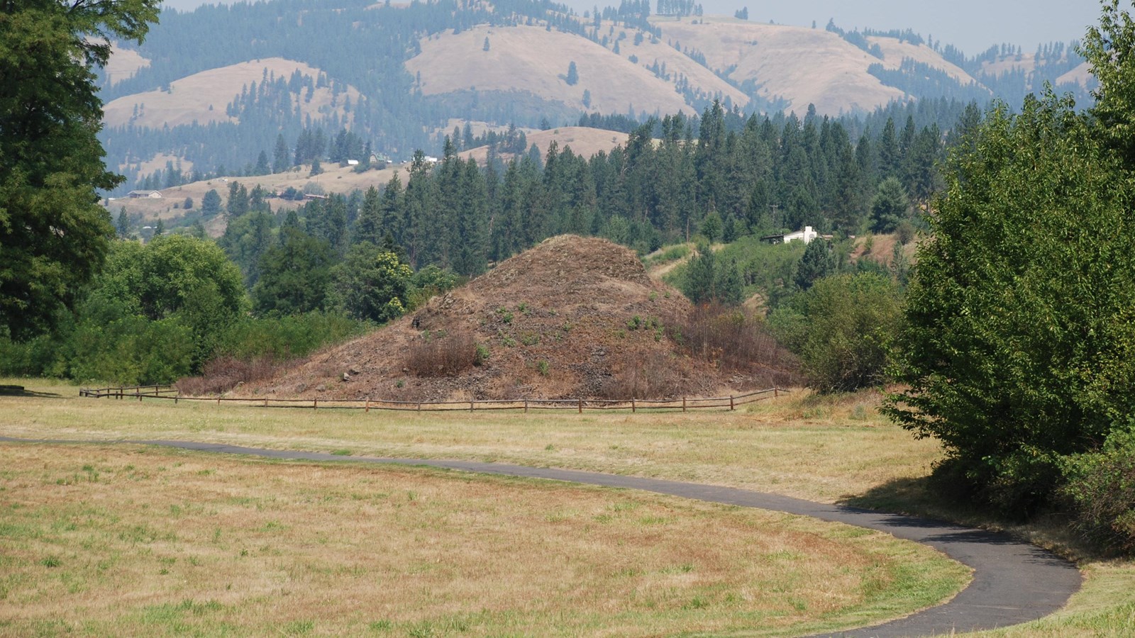A grass-covered mound, representing the heart of an ancient monster, sits along a paved trail.