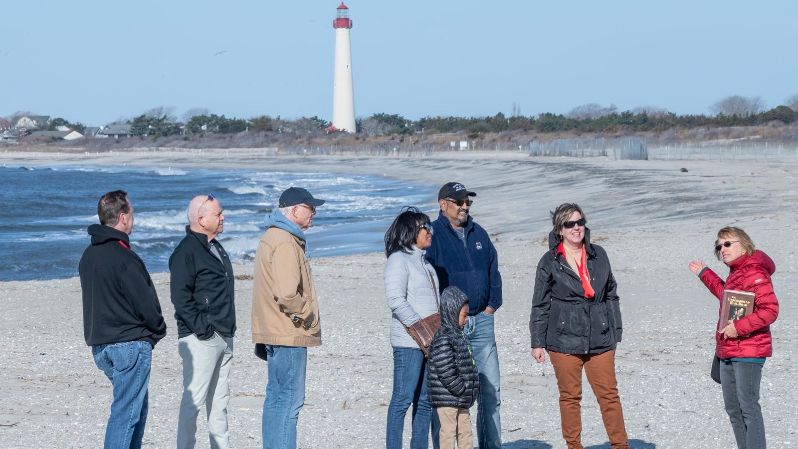 Visitors on a tour at South Cape May Meadows Beach with the lighthouse in the background