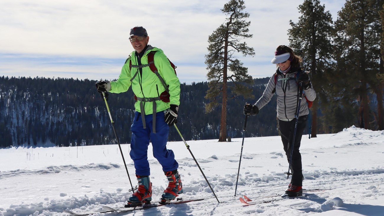 Two people on cross-country skis glide down a snowy, groomed path.