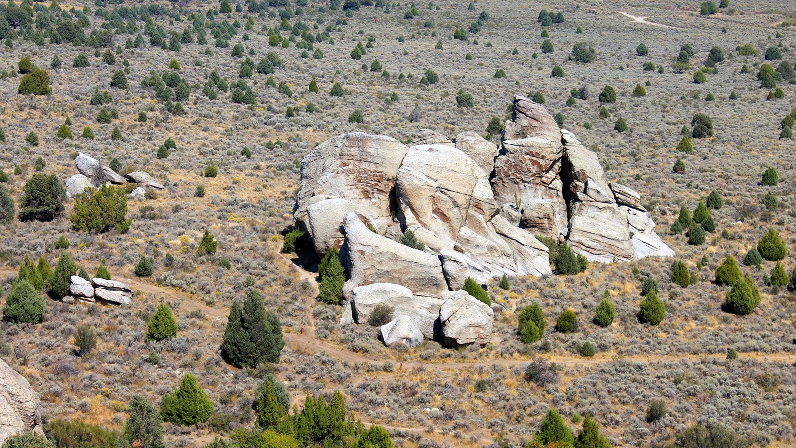 Granite formation in an open landscape with sage brush and juniper trees.