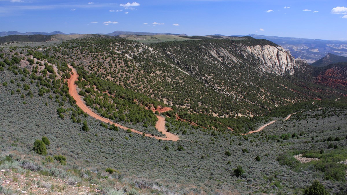 a red colored dirt road winds down a steep slope