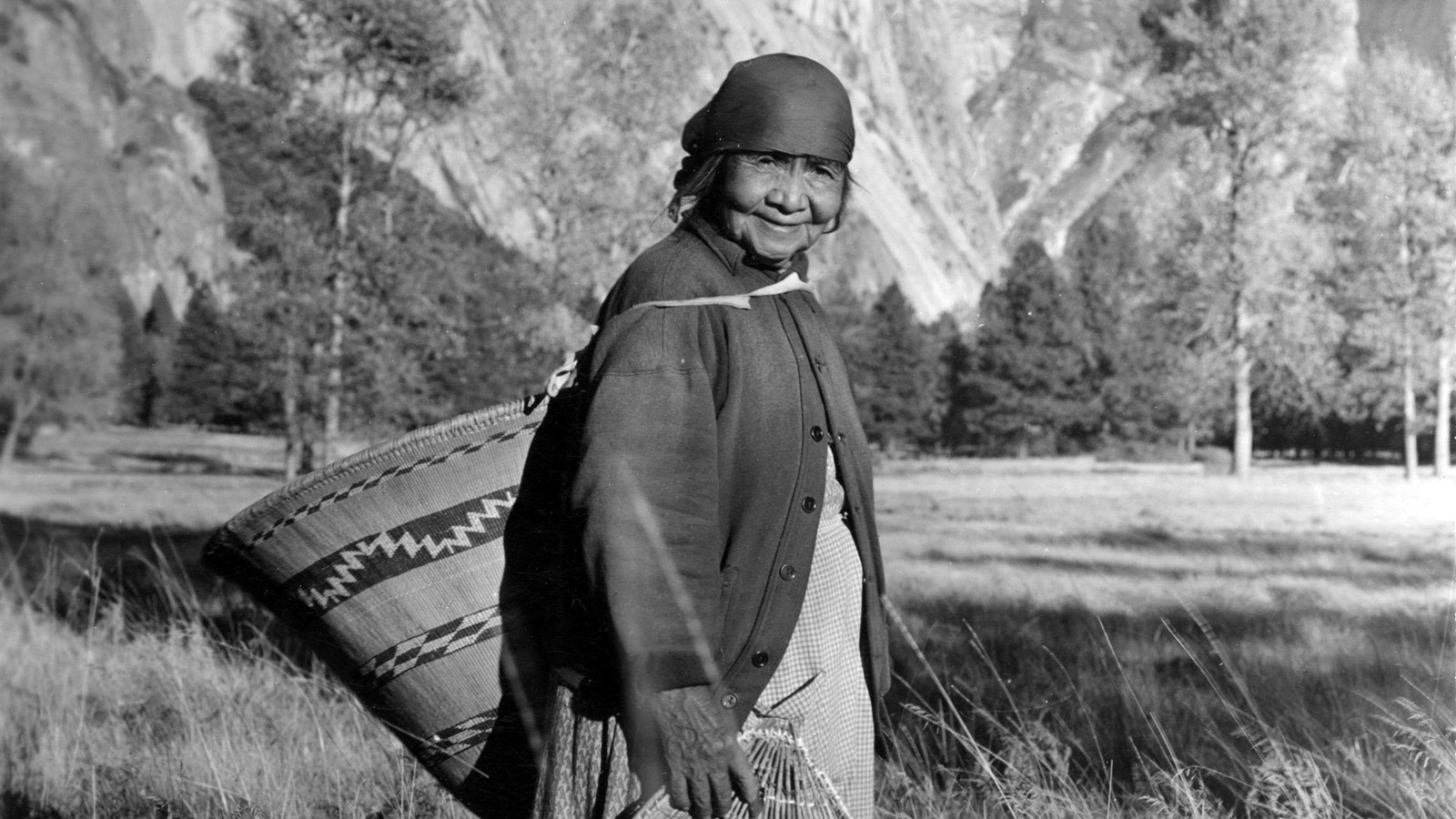 A Yosemite Indian woman carries baskets in Cook\'s Meadow