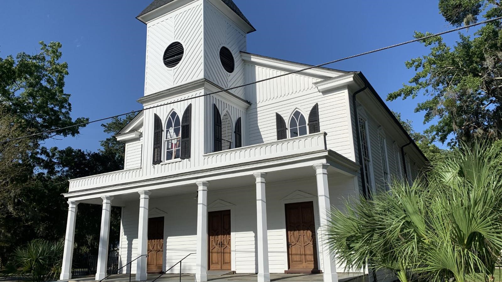 A two story gothic style white church with black shutters