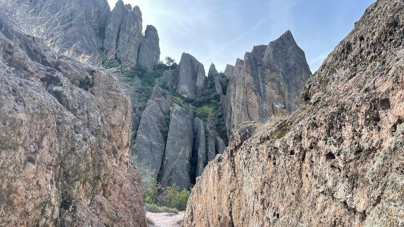 Trail passing through low rock walls with steep rock cliffs towering ahead.