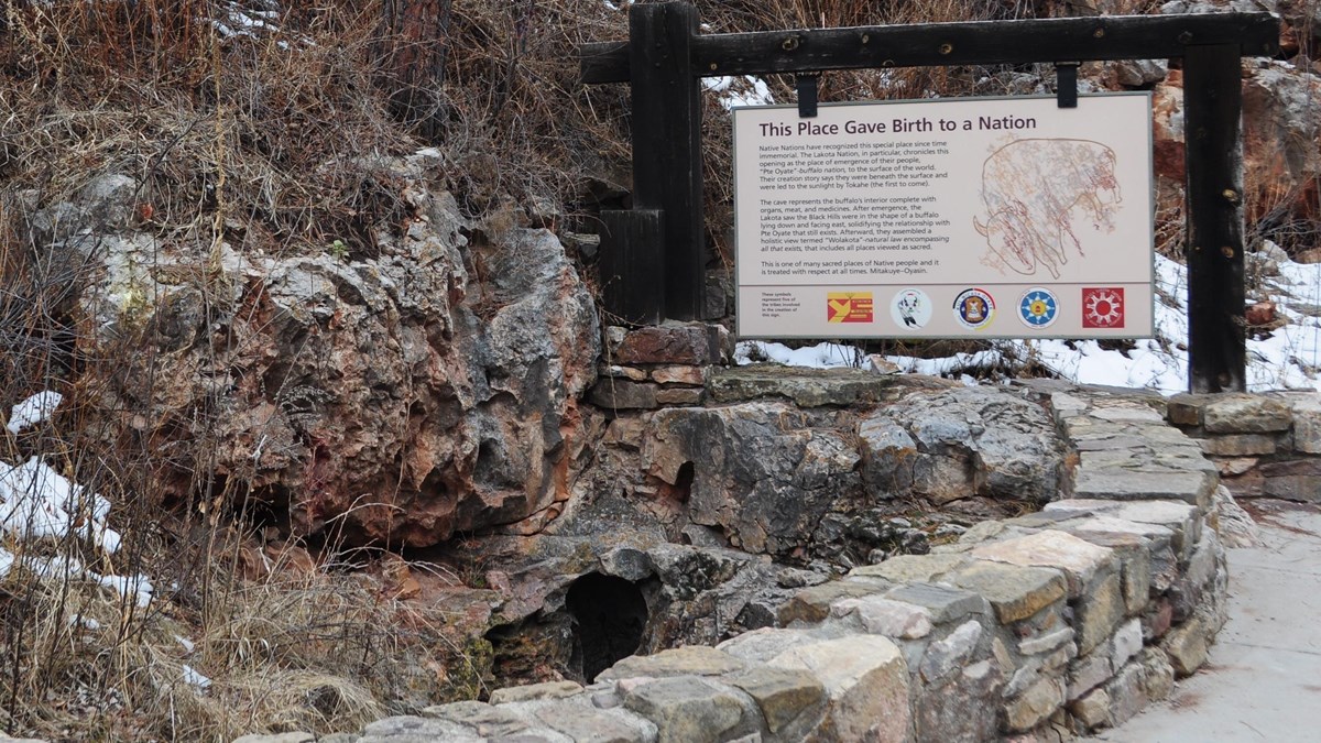 a small hole in a stone depression next to a large sign and short rock wall