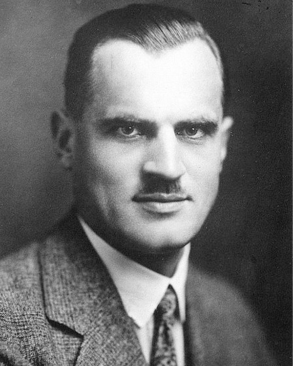 A black and white portrait photo of a mustached man.
