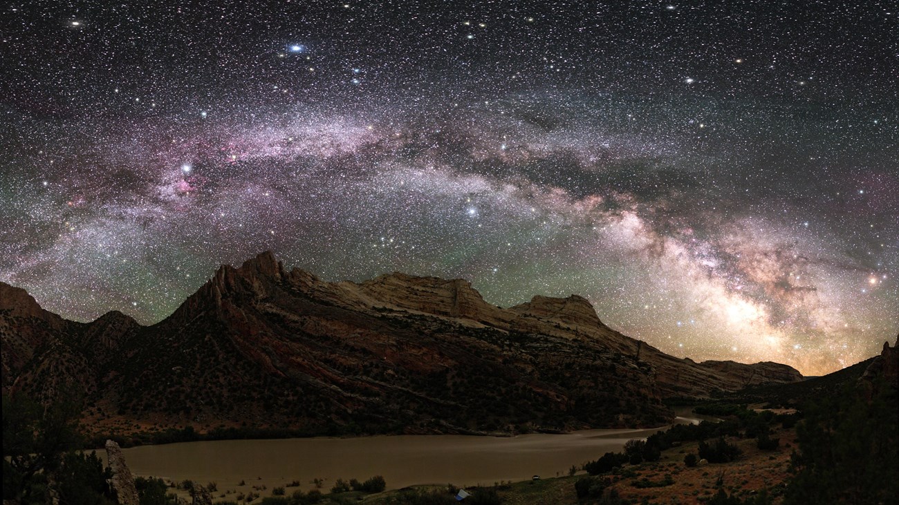 A band of brightly lit stars sweeps across the sky above a mountain.