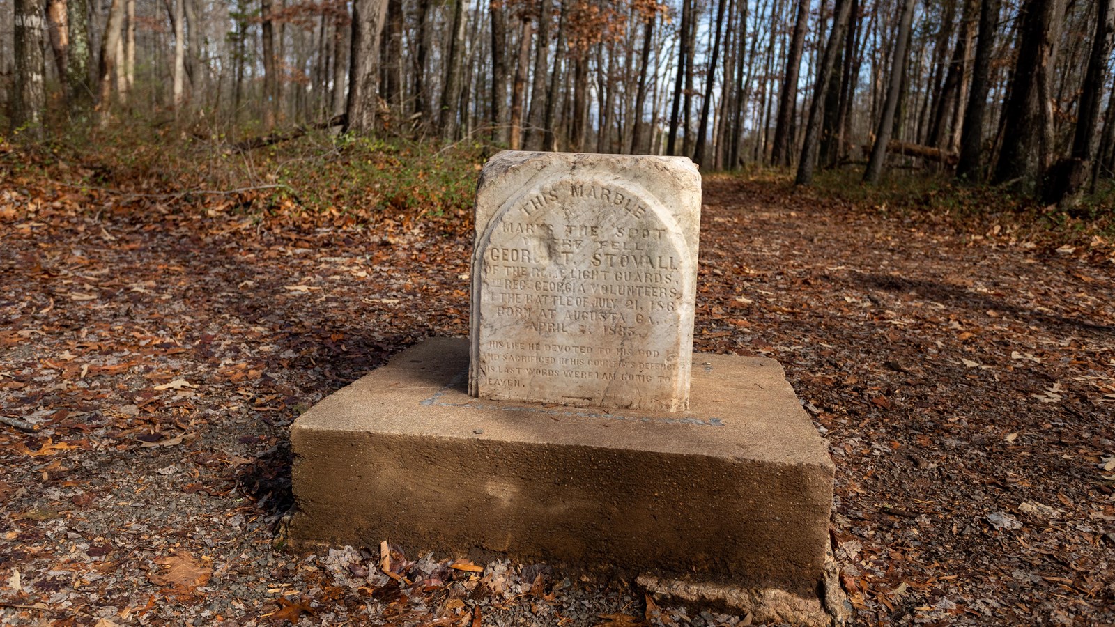 A white stone has faded, engraved text on its face. The stone sits atop a cement stand.