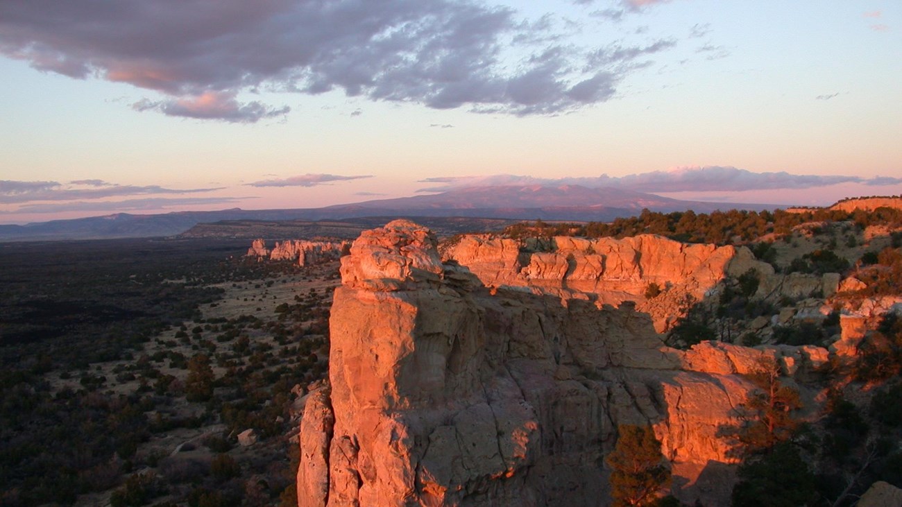 a tall sandstone bluff colored red by sunset under a darkening sky