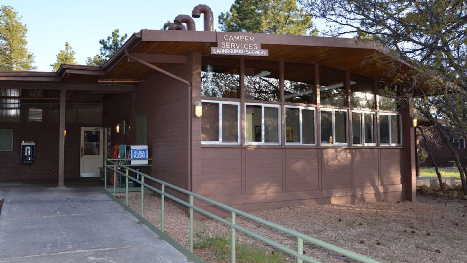 A ramp with a guardrail leads up to a L shaped brown building with windows.