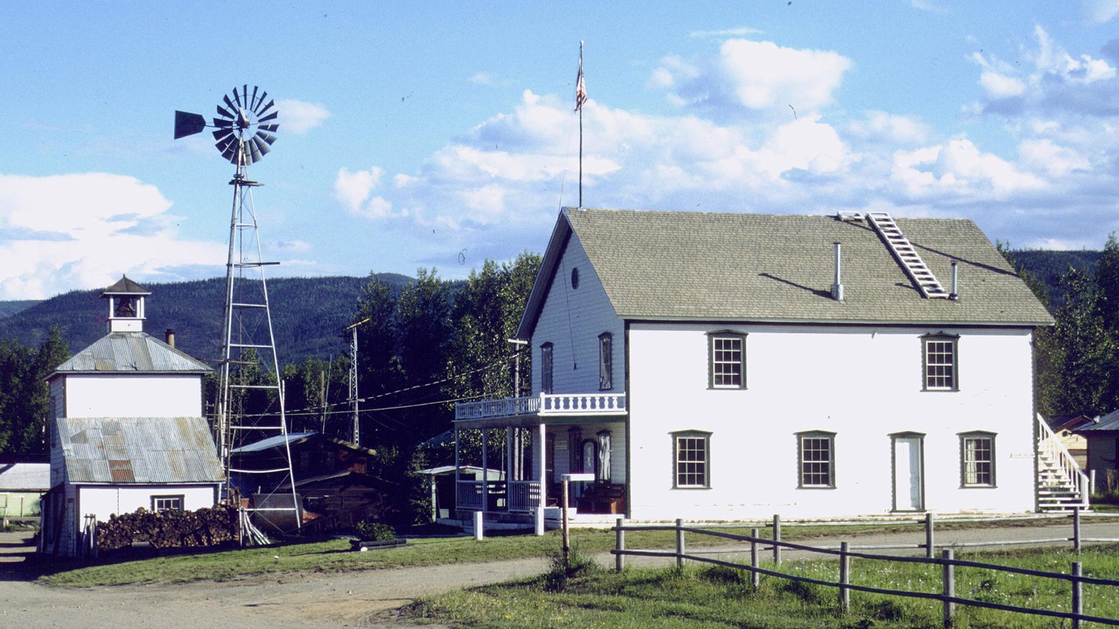 A two story white building with a gray roof and a two story, white, water pumping station.